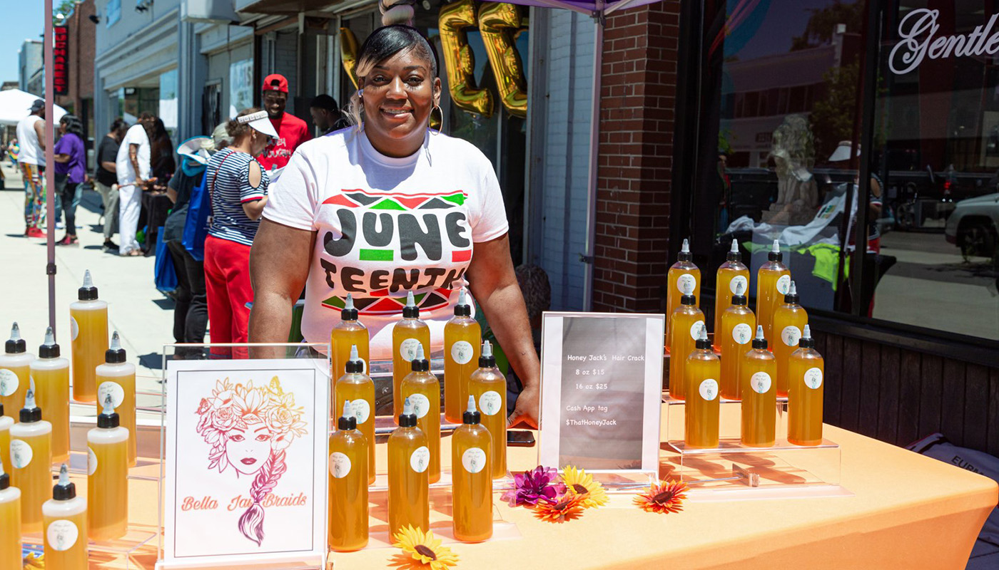 Woman standing outside behind table wearing a Juneteenth t-shirt, selling hair products in Detroit, MI