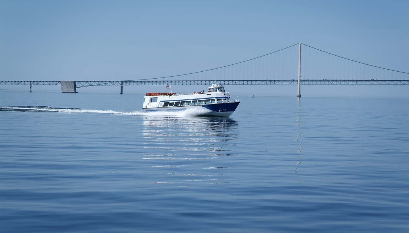 A ferry sails through the water in front of a large suspension bridge. 