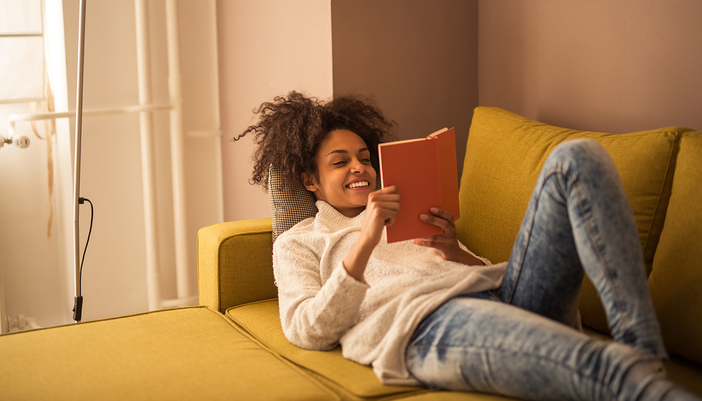 Young African American woman lounges on sofa, enjoying a book
