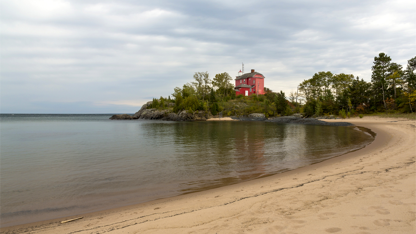 A red and white lighthouse and a sandy beach along Lake Superior in Michigan