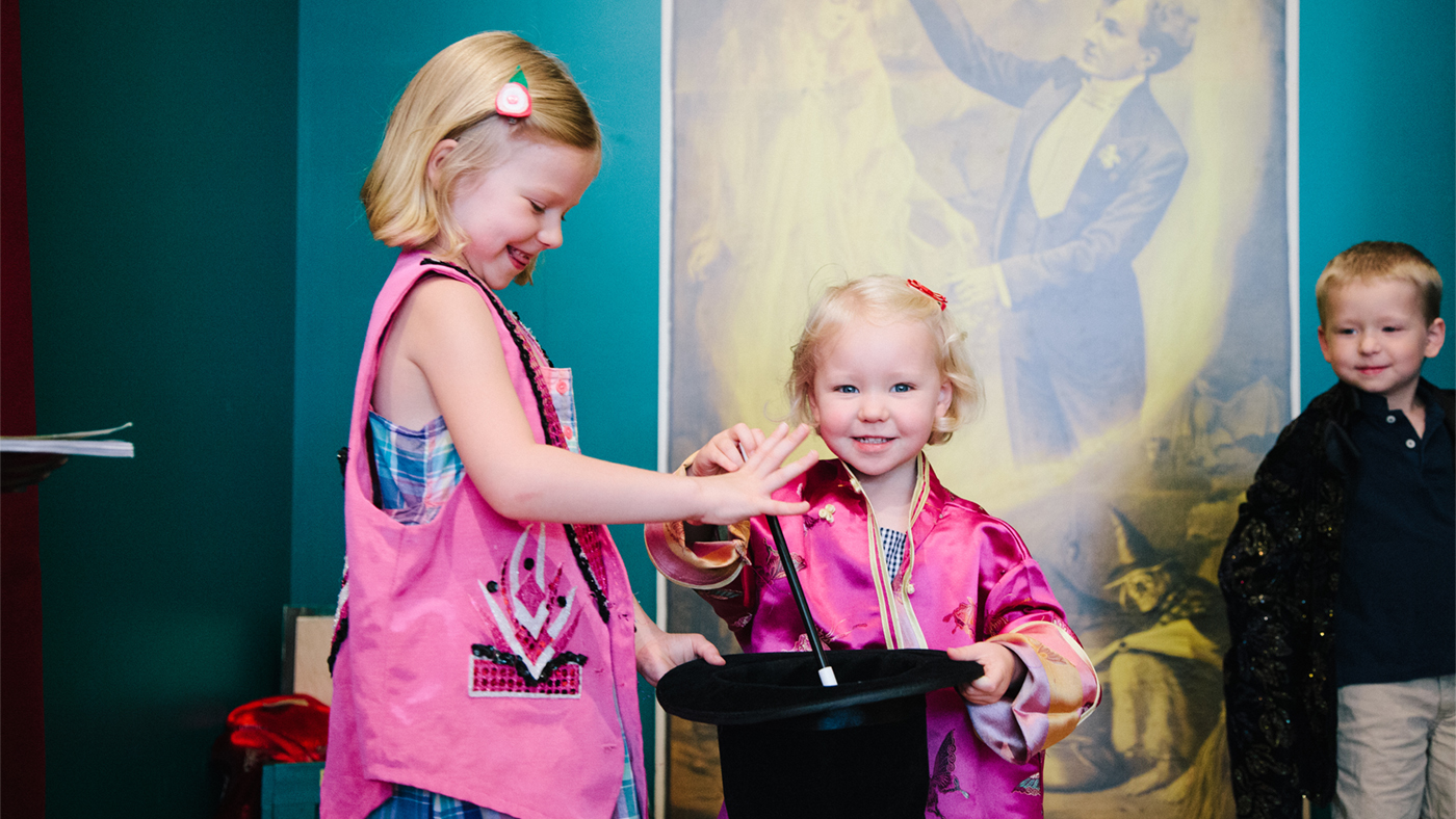Two young girls play with a magician’s hat and wand at the American Museum of Magic