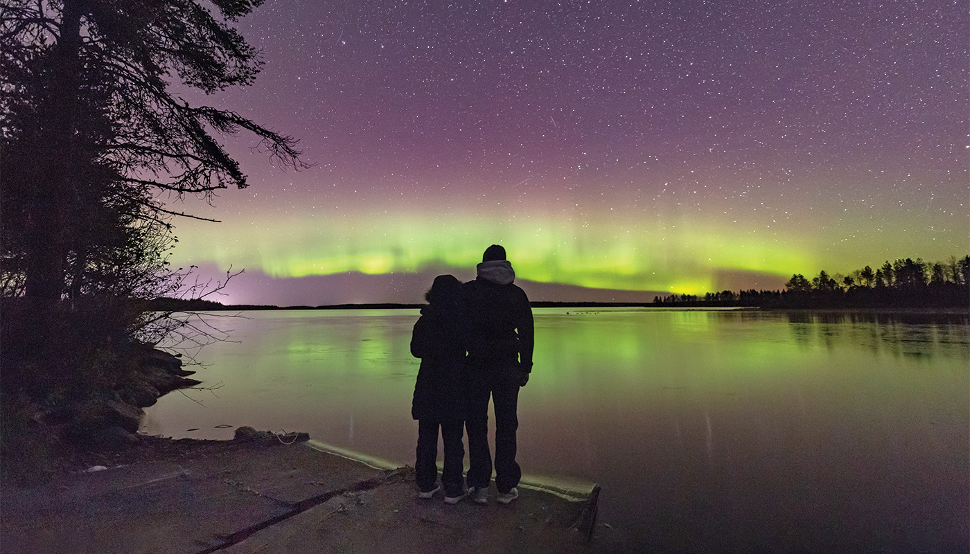 Couple looking at purple and green Northern Lights over Lake Kuusamo, Pohjois-Pohjanmaa, Finland