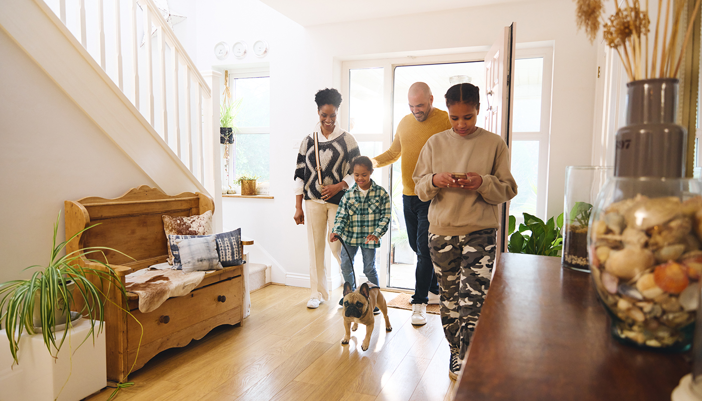 Two adults, a teenager, a child and dog enter the foyer of a home.