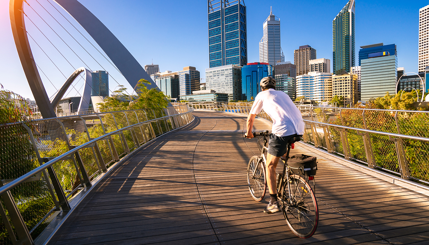 A man rides a bicycle along a path with several tall buildings in the background.