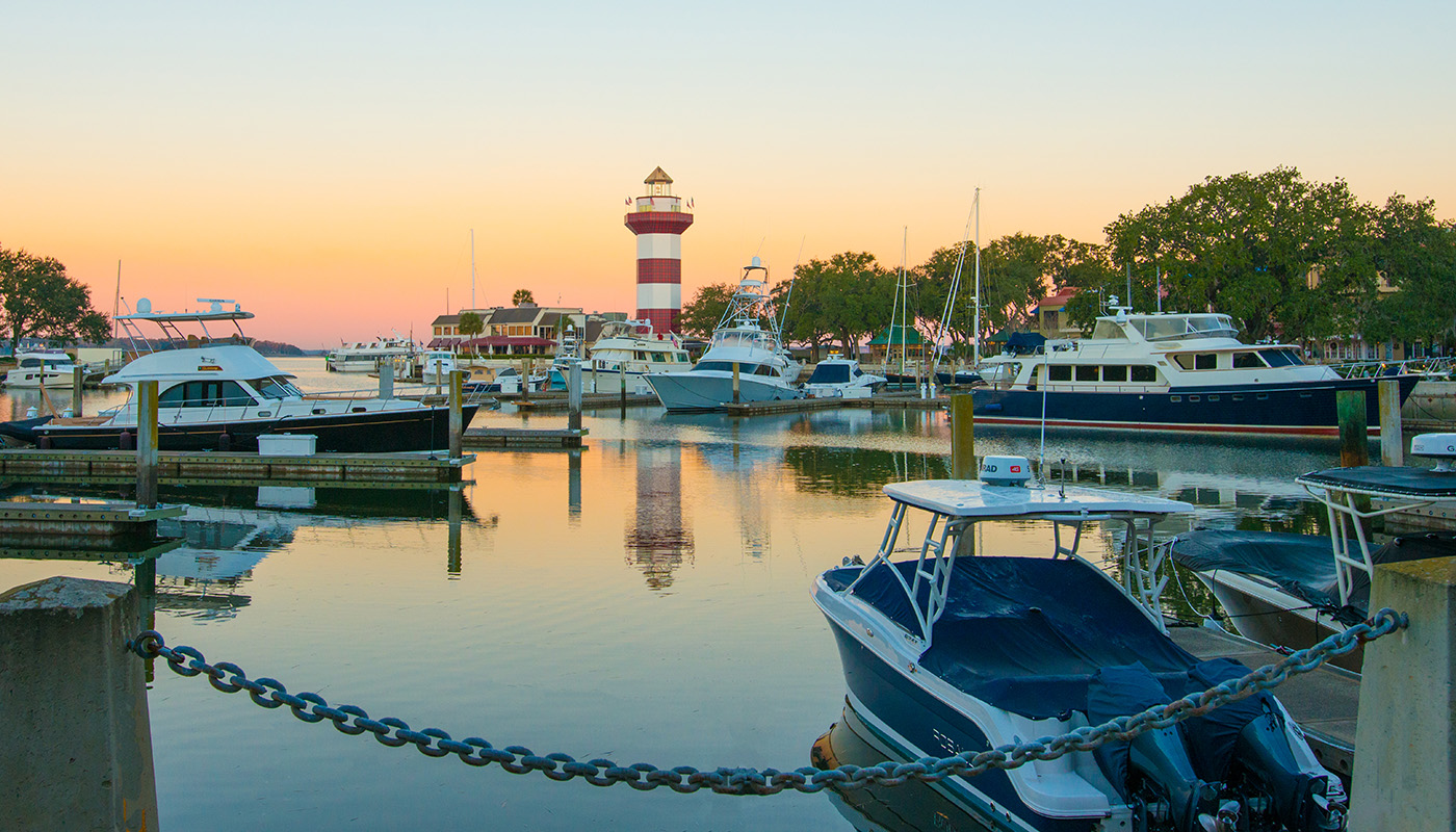 Sunrise behind the lighthouse at Harbour Town with boats parked at dock in the foreground