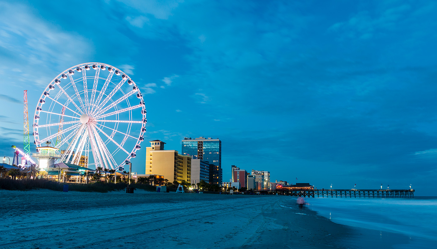SkyWheel ferris wheel illuminated against evening sky, next to shoreline in Myrtle Beach, South Carolina