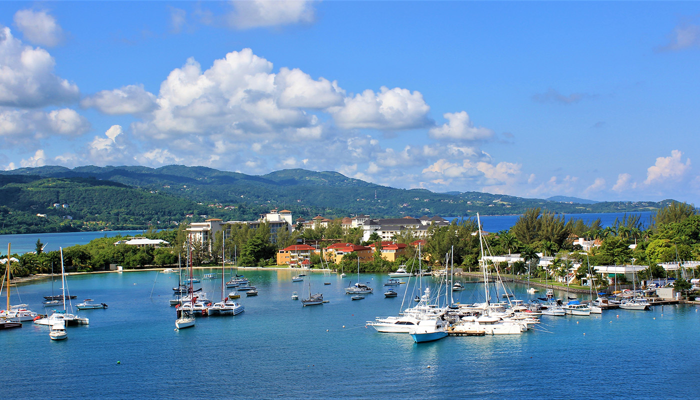 View of Jamaica from Montego Bay. Multiple boats of varying sizes float in the foreground.