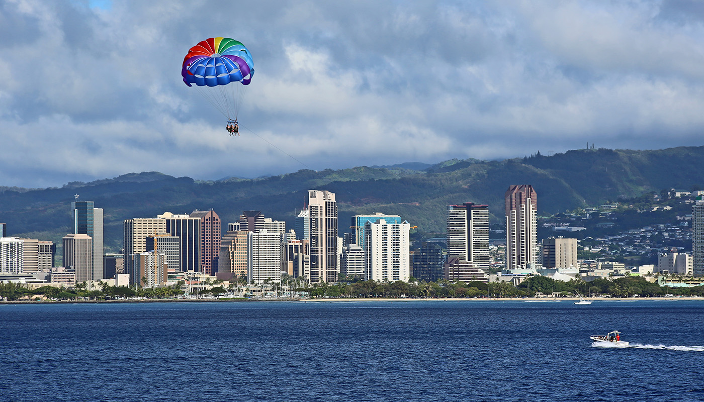 Boat pulls parasailer over water with skyline of Oahu, Hawaii in background