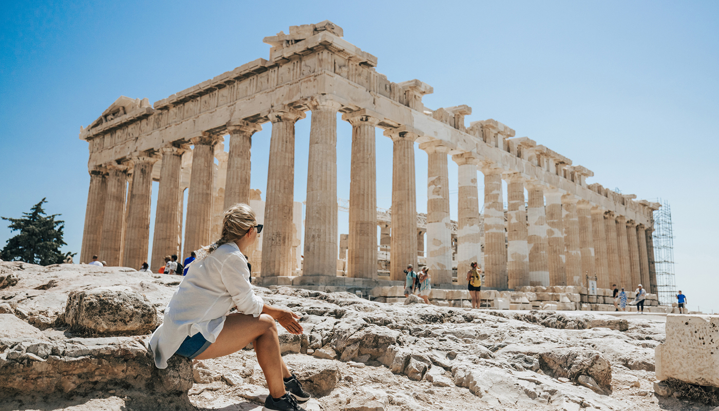 Woman relaxing while looking at Parthenon temple against clear sky during sunny day