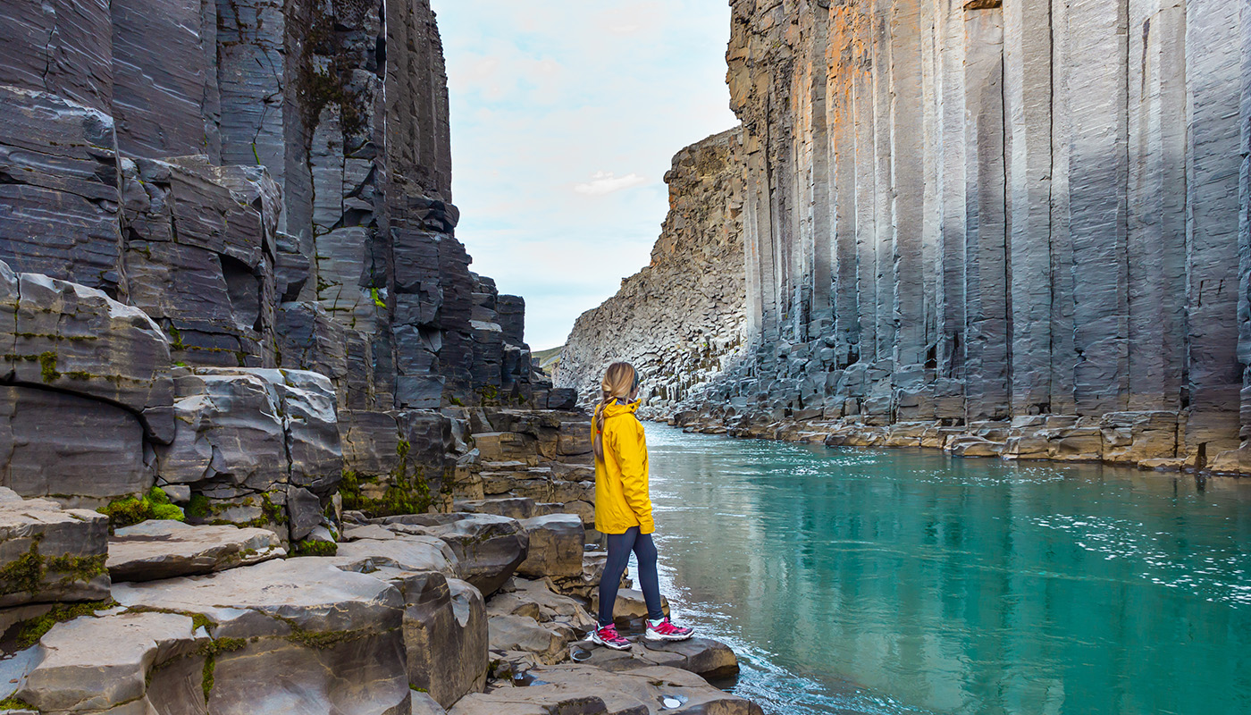 A hiker stands next to blue-green water at the bottom of a canyon