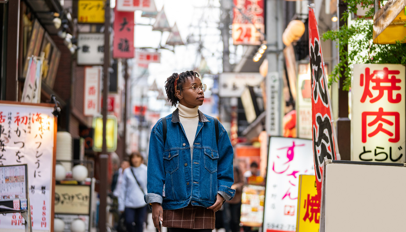 A traveler walks through a busy street that’s crowded with signs.