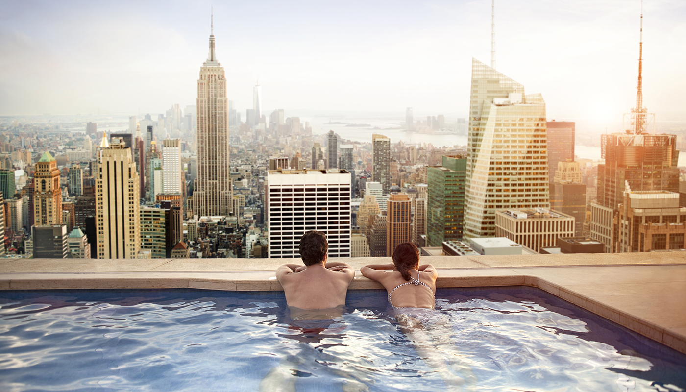 A man and woman in a pool at the top of a building, taking in the view of the city.