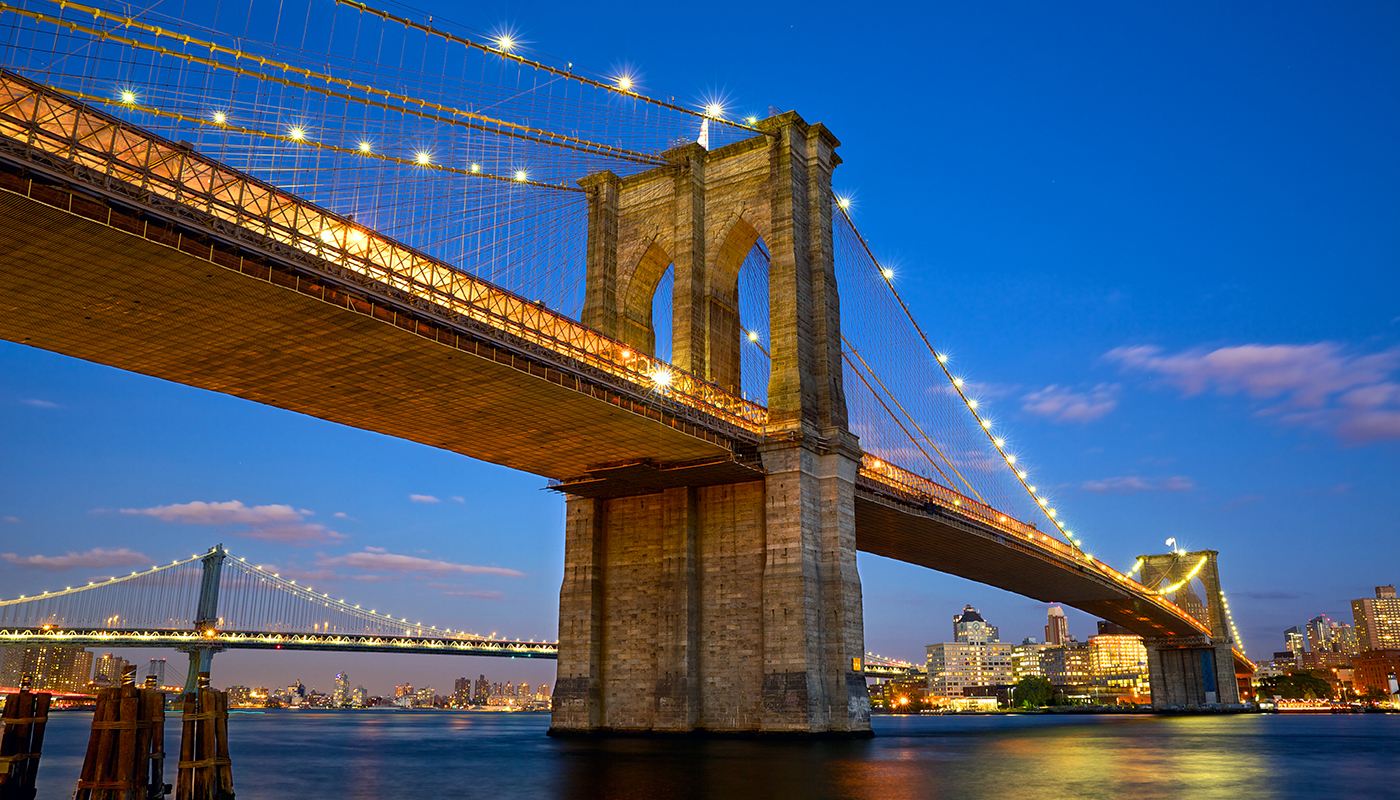 Brooklyn Bridge lit up at night over the East River.