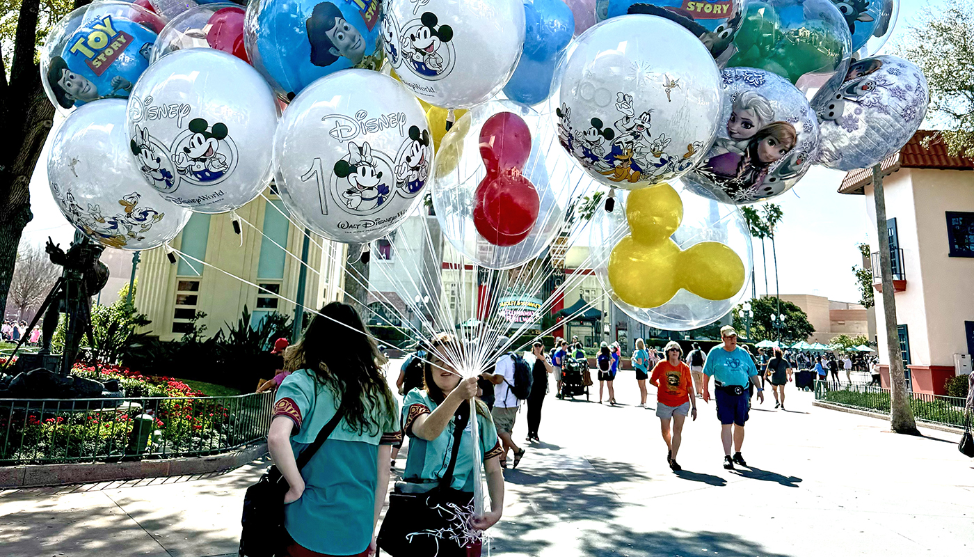 A Disney park employee holds a giant spray of balloons featuring popular Disney characters