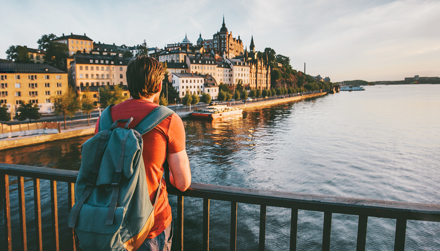 A man wearing a backpack stands on a bridge and looks across the water