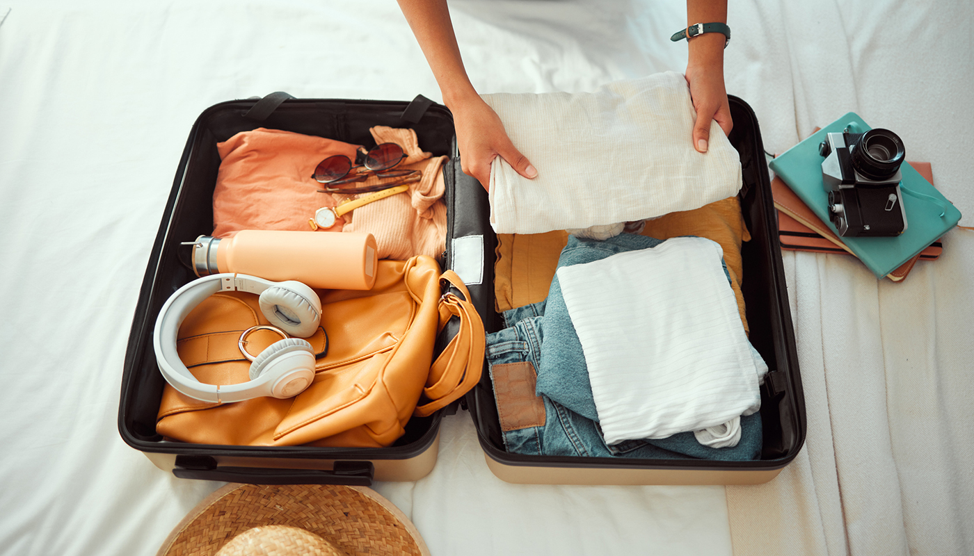 A woman packs her clothes, headphones, water bottle and camera in her suitcase