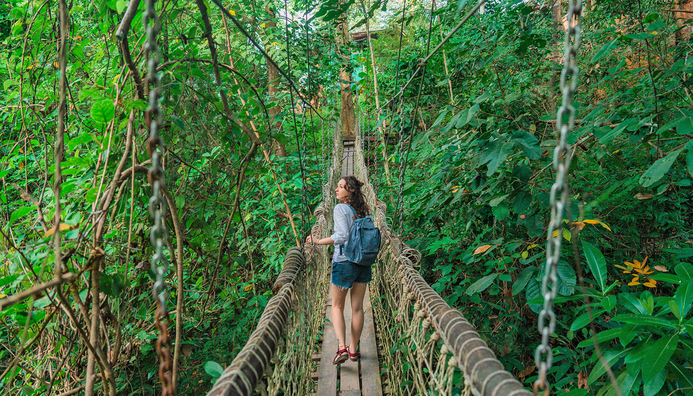 A woman crosses a bridge suspended in a forest of trees and foliage