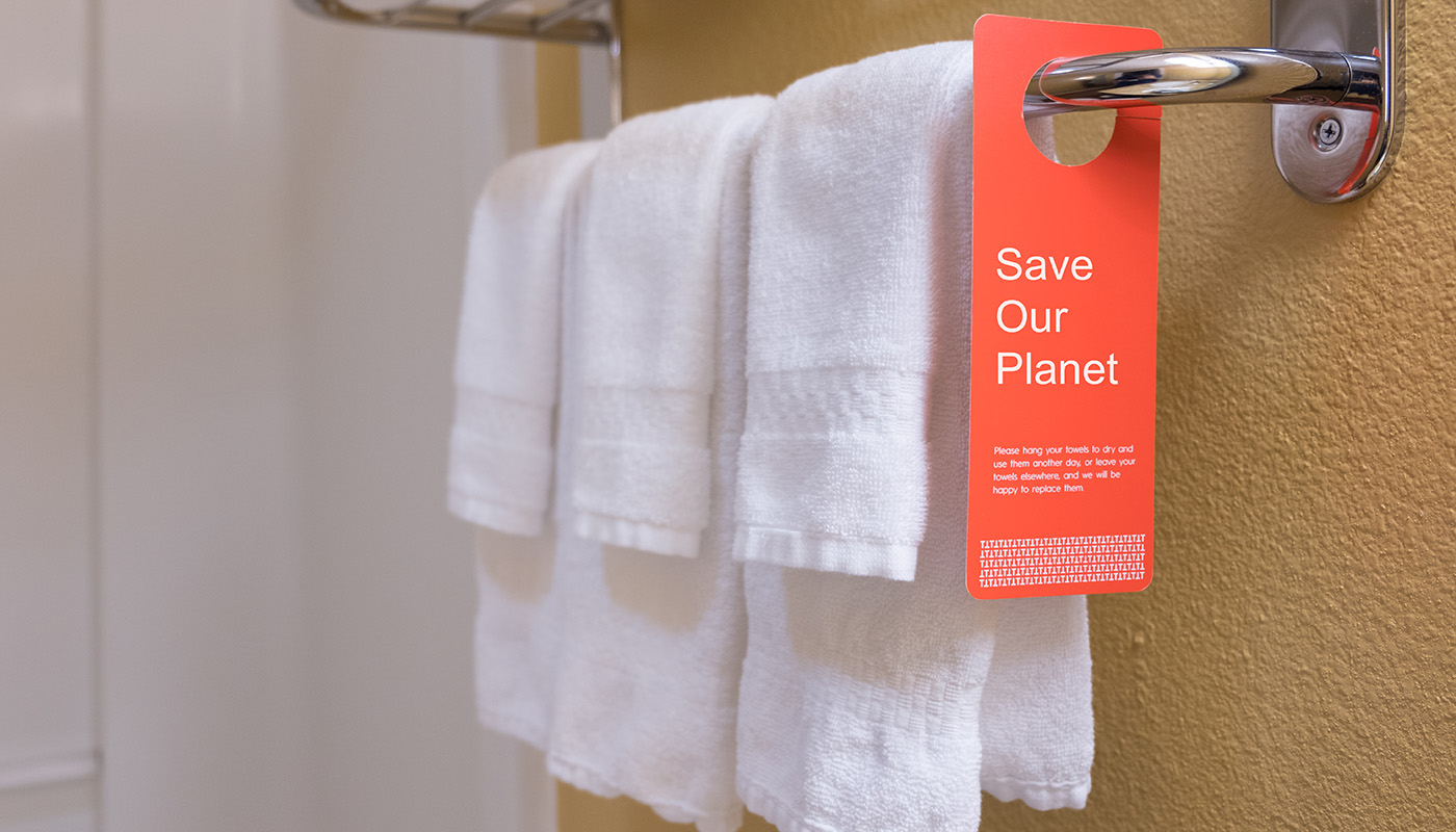 Towels hanging in hotel bathroom with tag that says Save Our Planet