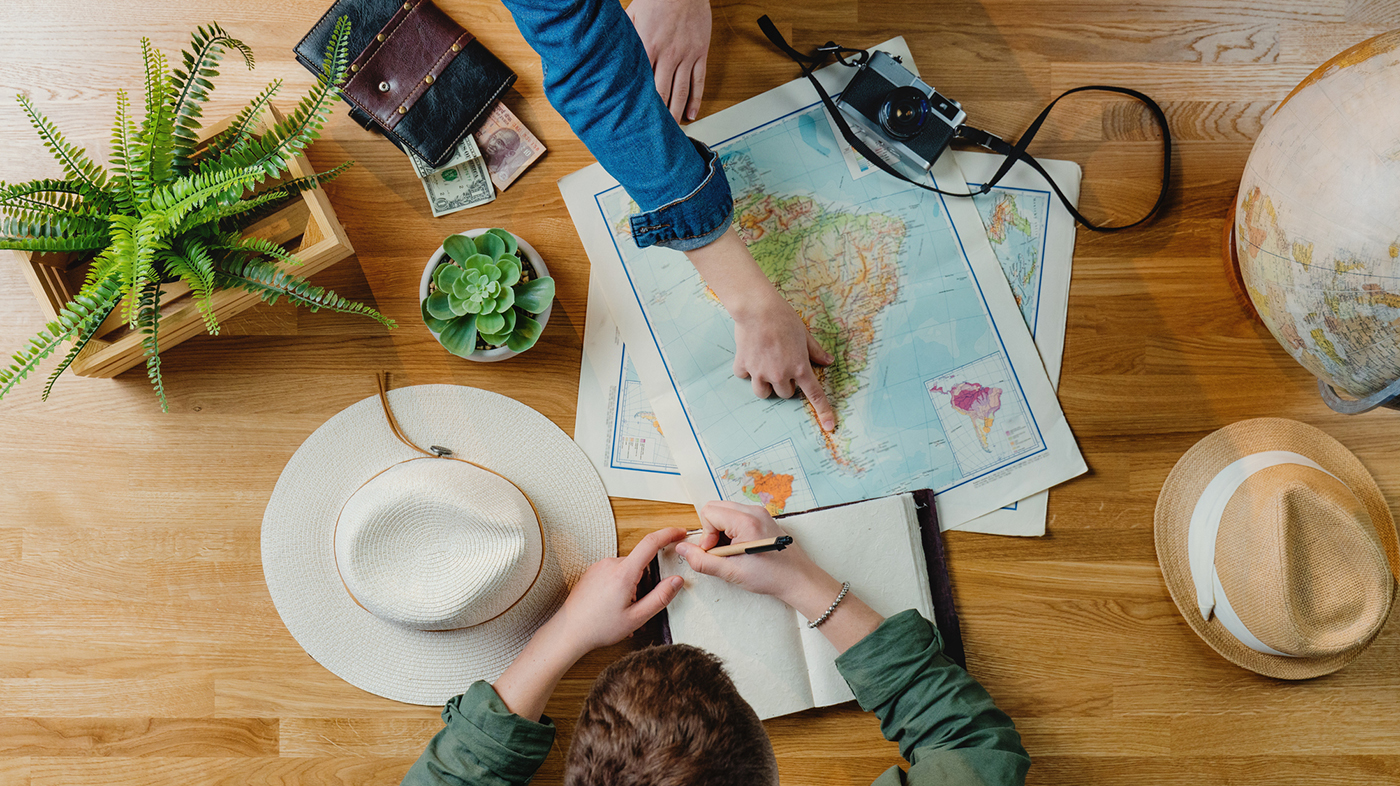 Top view of unrecognizable young couple with maps planning vacation trip holiday, desktop travel concept.