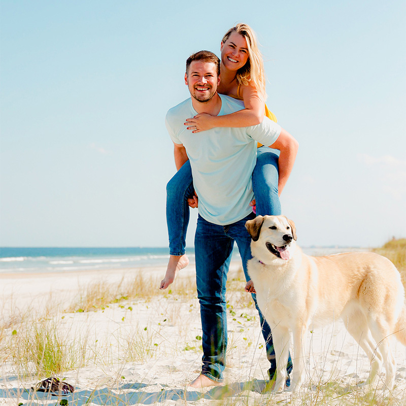Jon and girlfriend with their dog on a beach.