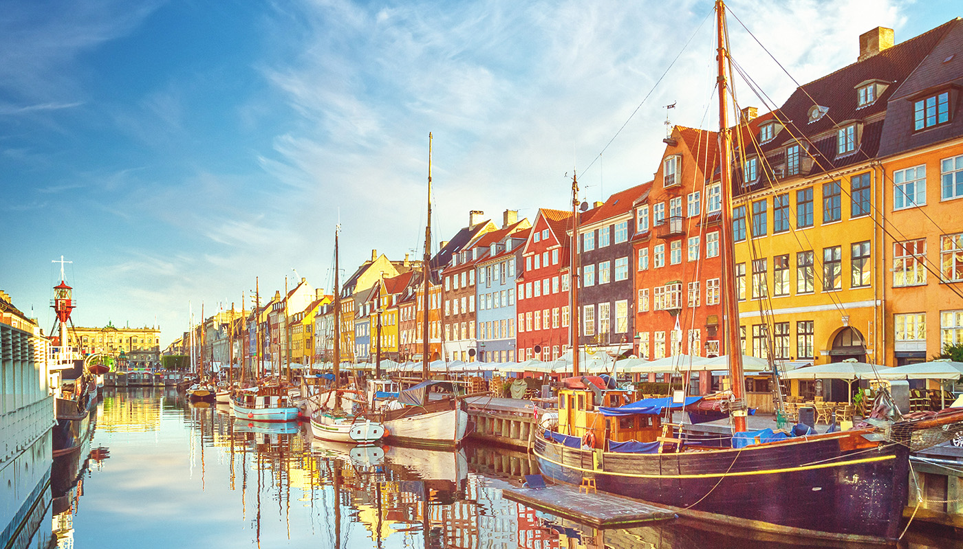 Colorful houses and bright blue sky along Nyhavn harbor with boats parked at dock