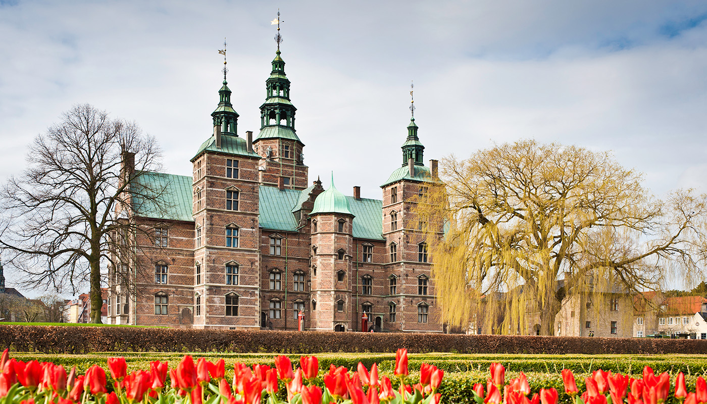 The renaissance spires of Rosenborg Castle overlooking the tranquil green oasis of Kongens Have, The King's Garden, with vibrant red tulips blooming in the spring sunshine