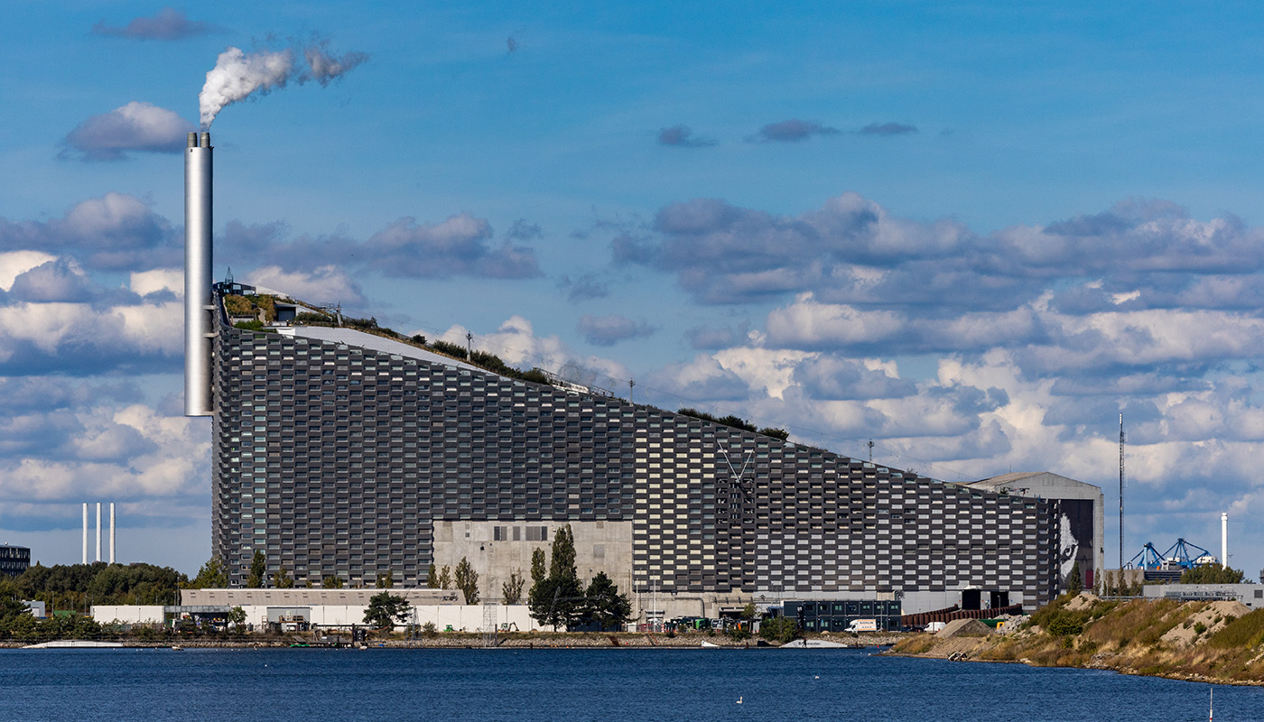 Exterior of CopenHill against bright blue sky with water in foreground