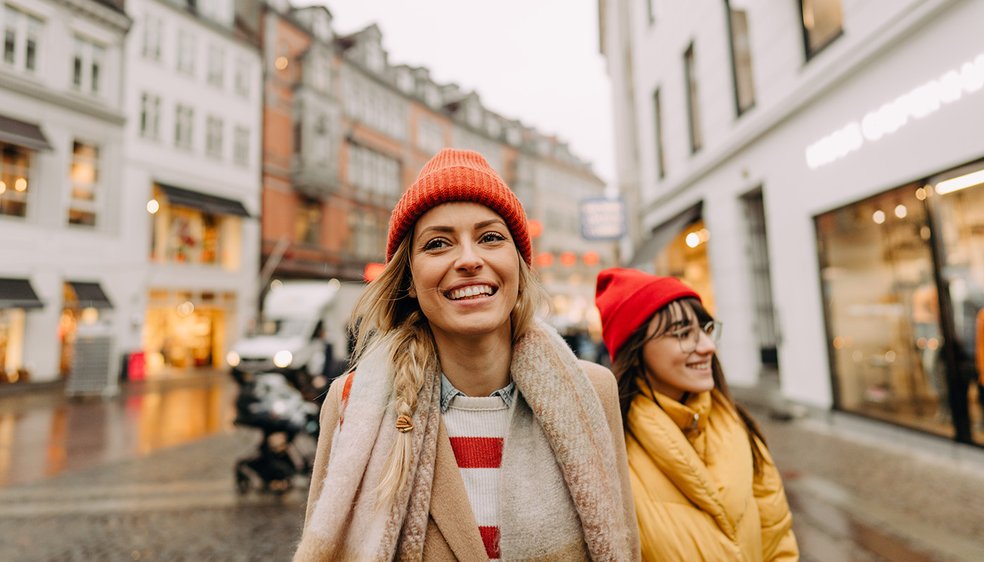 Two smiling women in hats and coats walk down a city street
