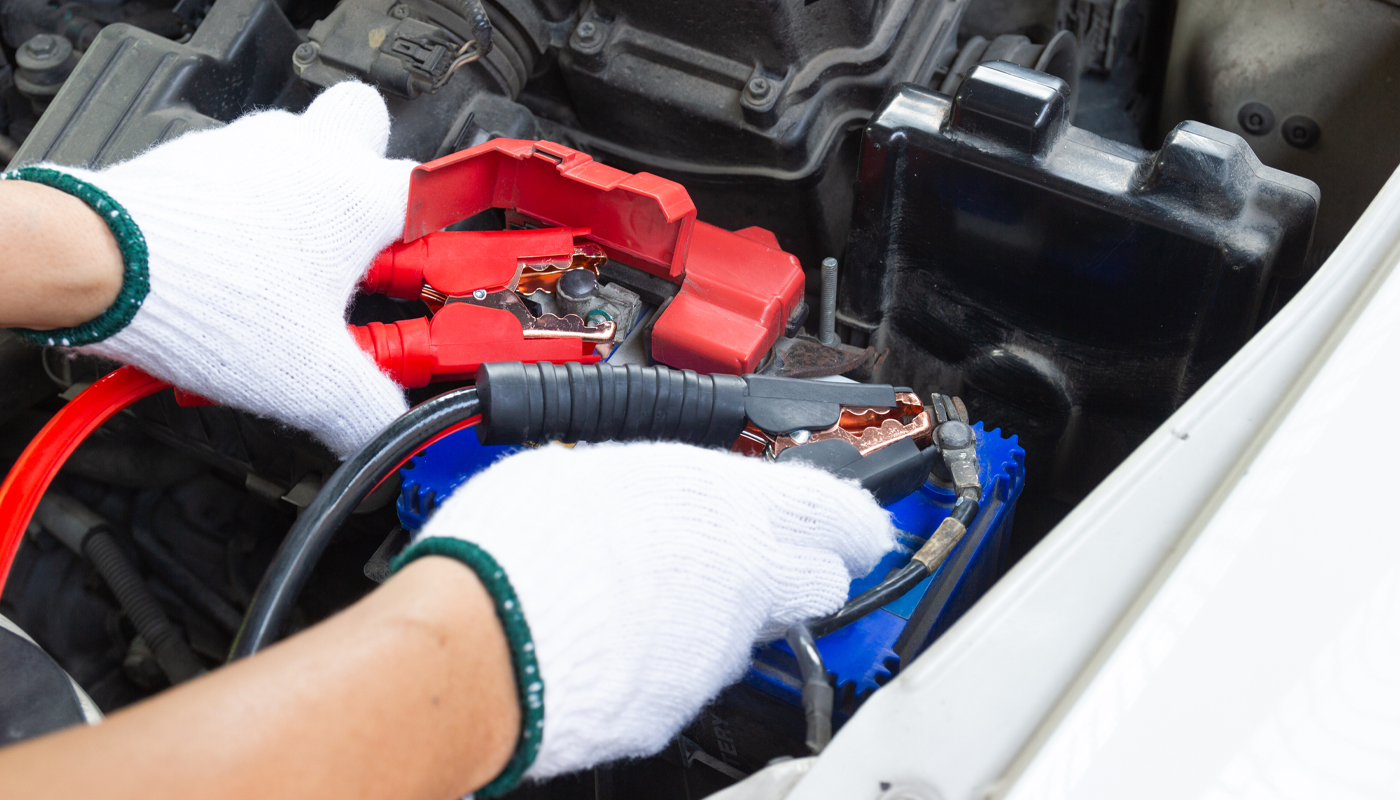 Person wearing gloves using jumper cables to charge car battery