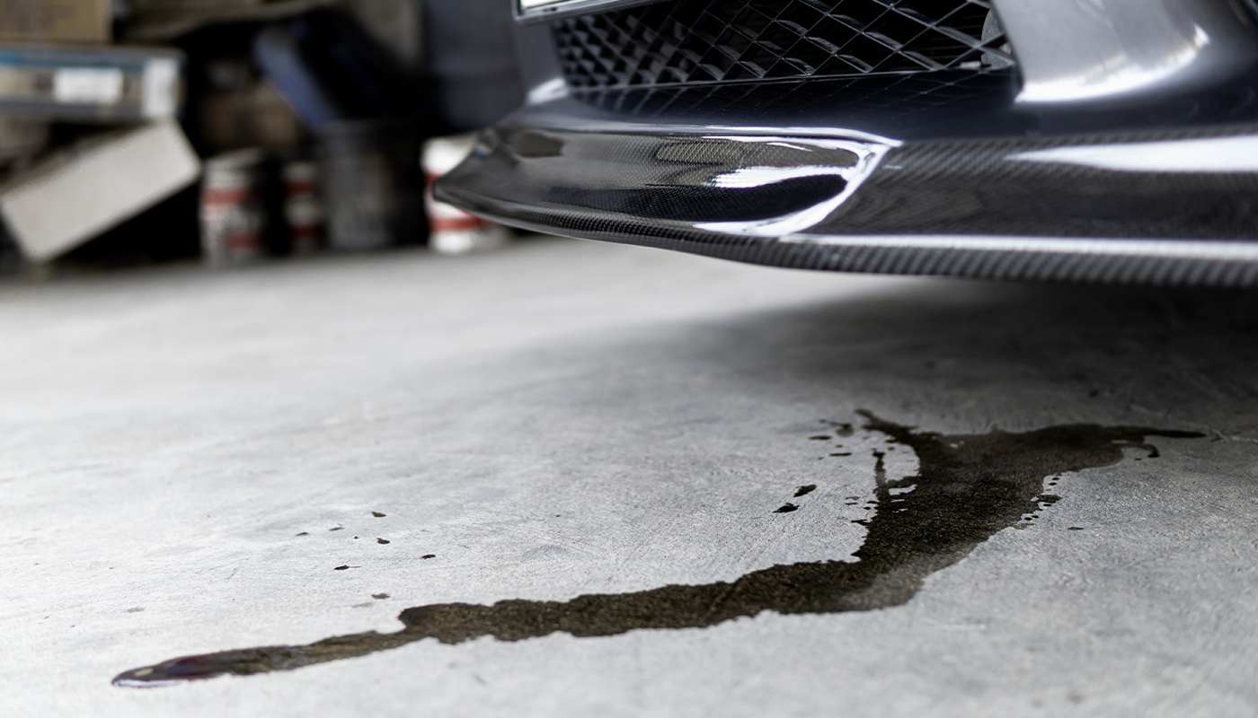 An engine oil leak runs on the concrete underneath a vehicle.