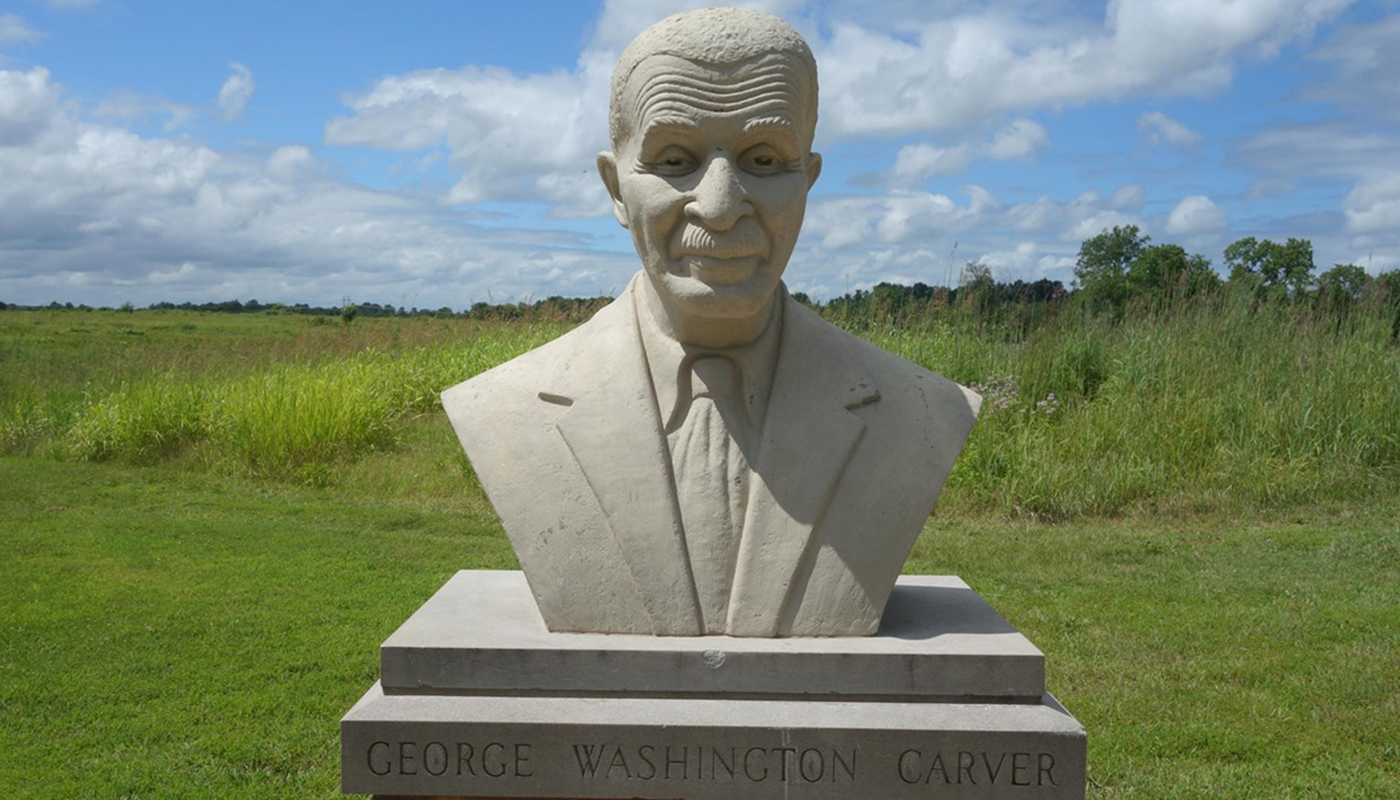 Statue bust of George Washington Carver with a lush green field in the distance