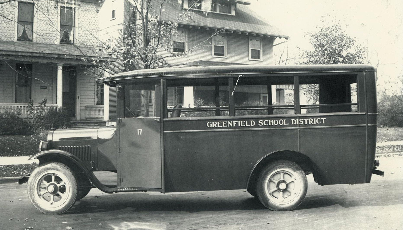One of the first Greenfield School District busses built by the C.R. Patterson & Sons Company on a street in front of a house