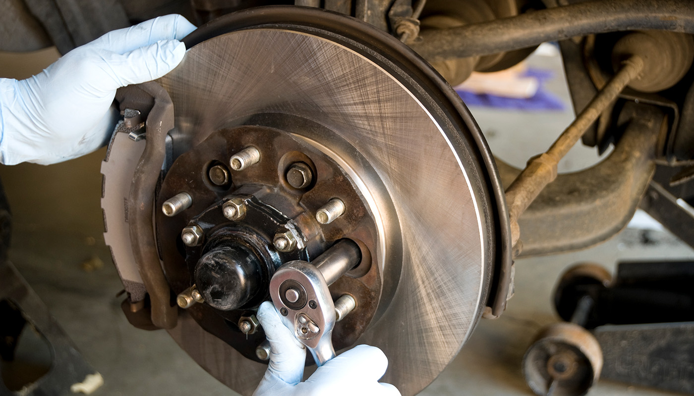 Closeup of gloved hands using a socket wrench to remove the bolts holding on the disc brake rotor and wheel hub