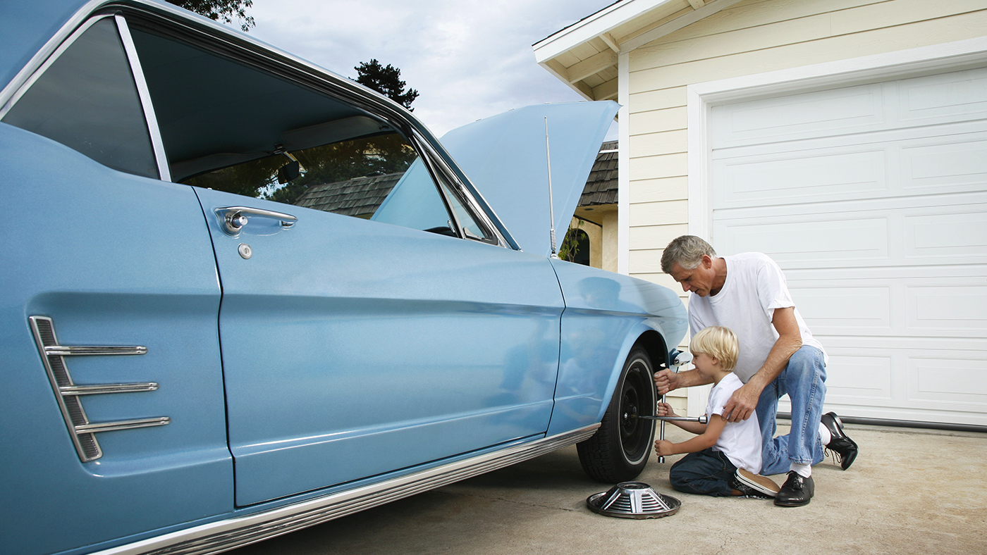 Father and son changing the tire of a vintage blue car in the driveway