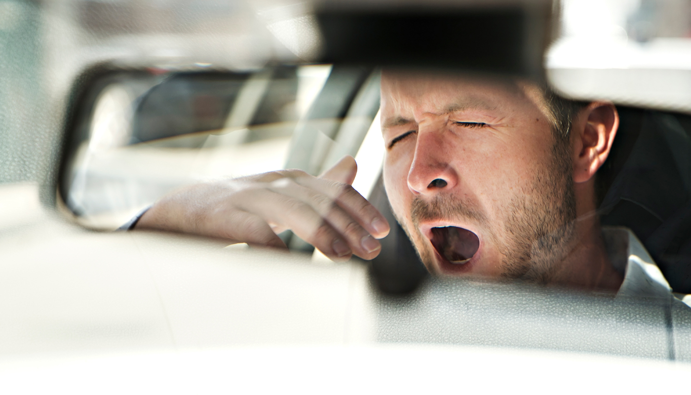 Reflection in rearview mirror of a man yawning in a car