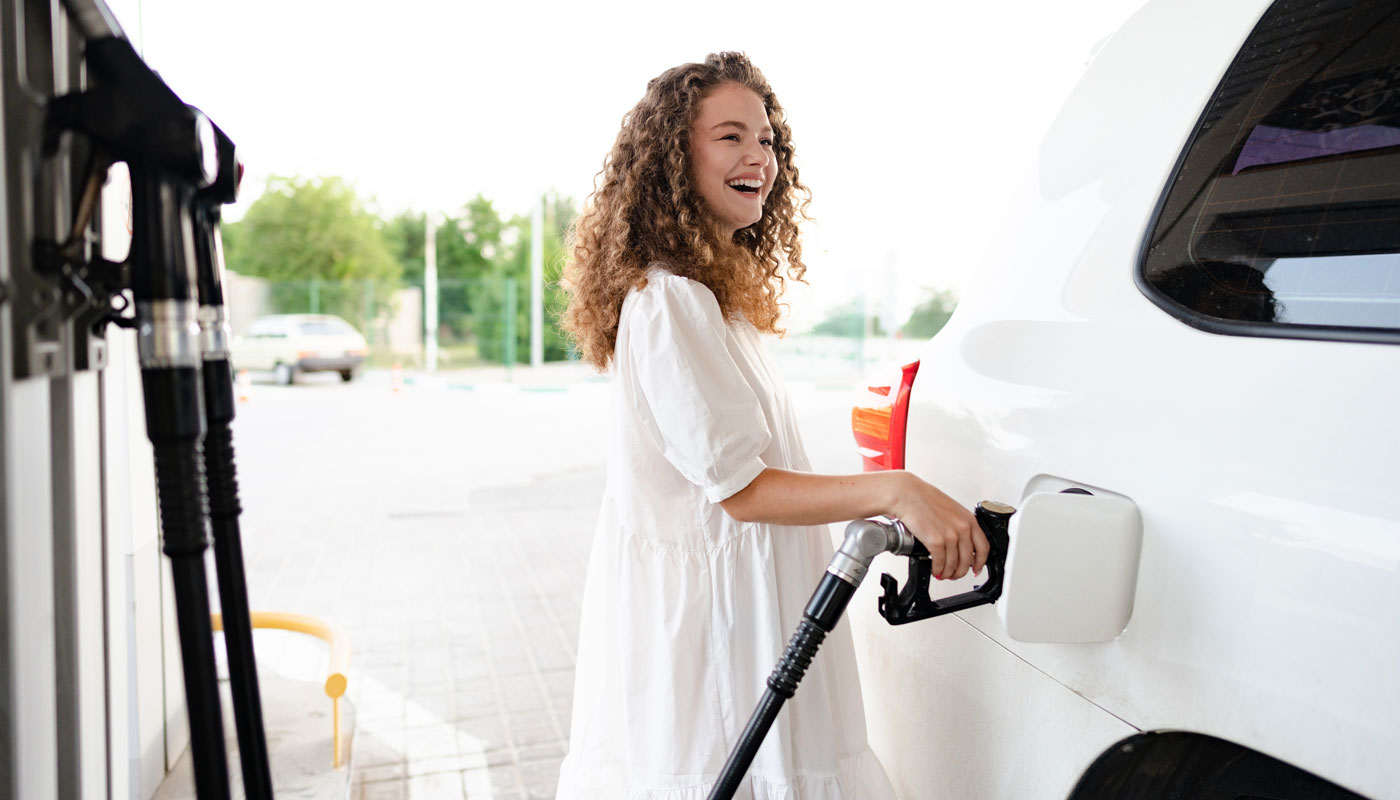 woman in white dress pumping gas at a station