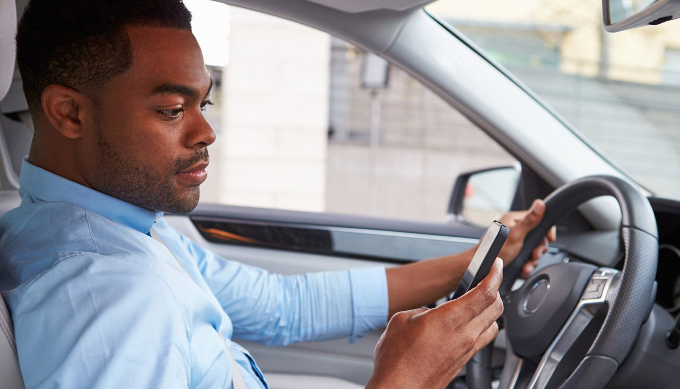 Man in driver's seat of car looking at mobile phone