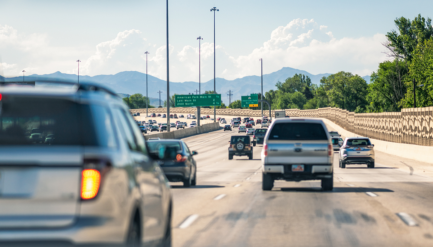 Various vehicles driving on an a busy highway with mountains off in the distance.