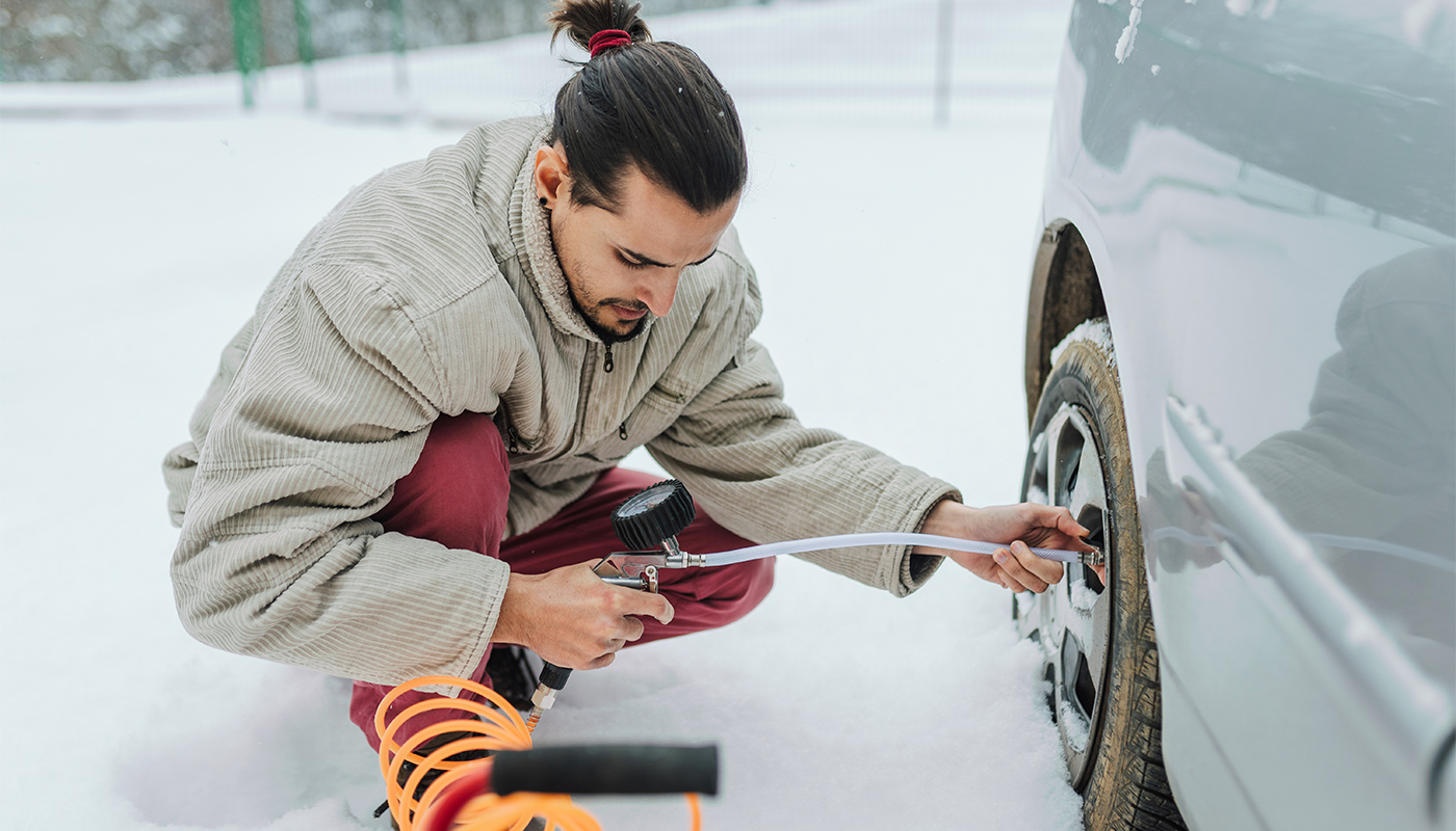 Young man Checking Tire Pressure during winter