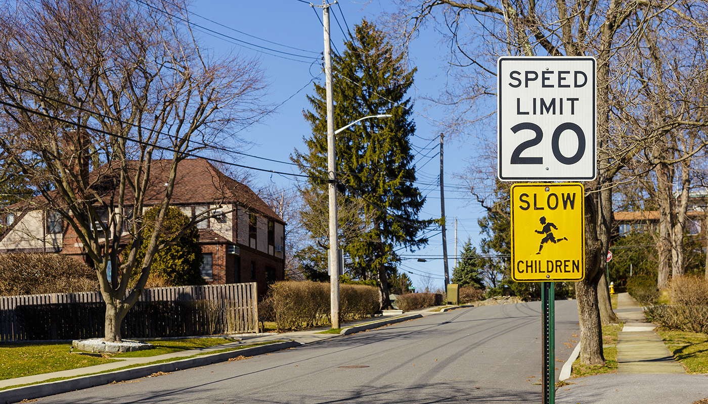Two signs read, “SPEED LIMIT 20” and “SLOW CHILDREN” on the side of a neighborhood street.