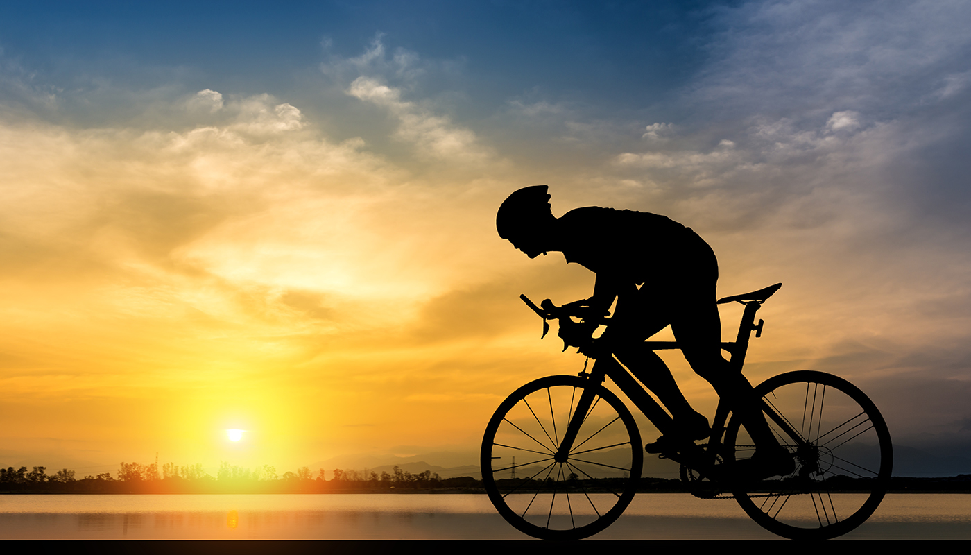 Silhouette of bicyclist riding bike along a body of water with sun setting in distance