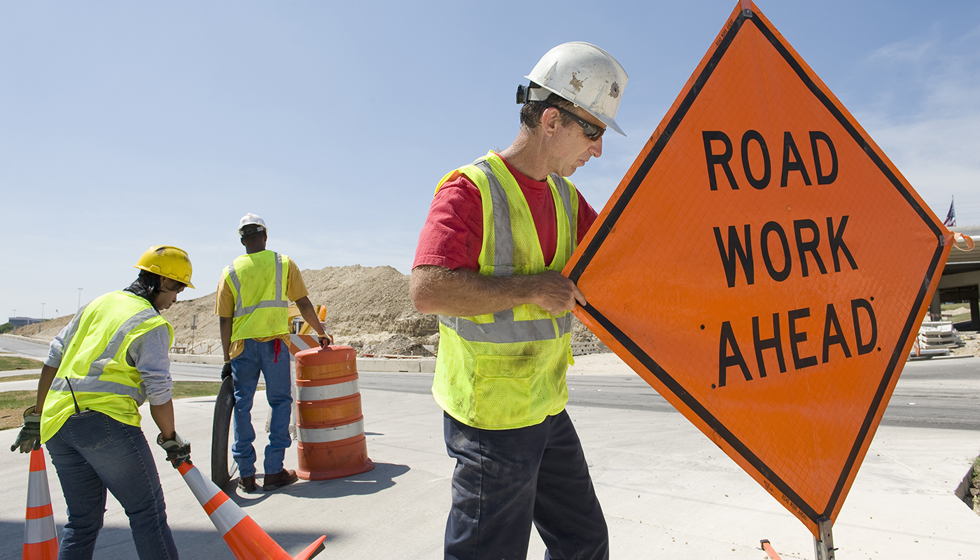 Road workers moving equipment and road signs on highway 