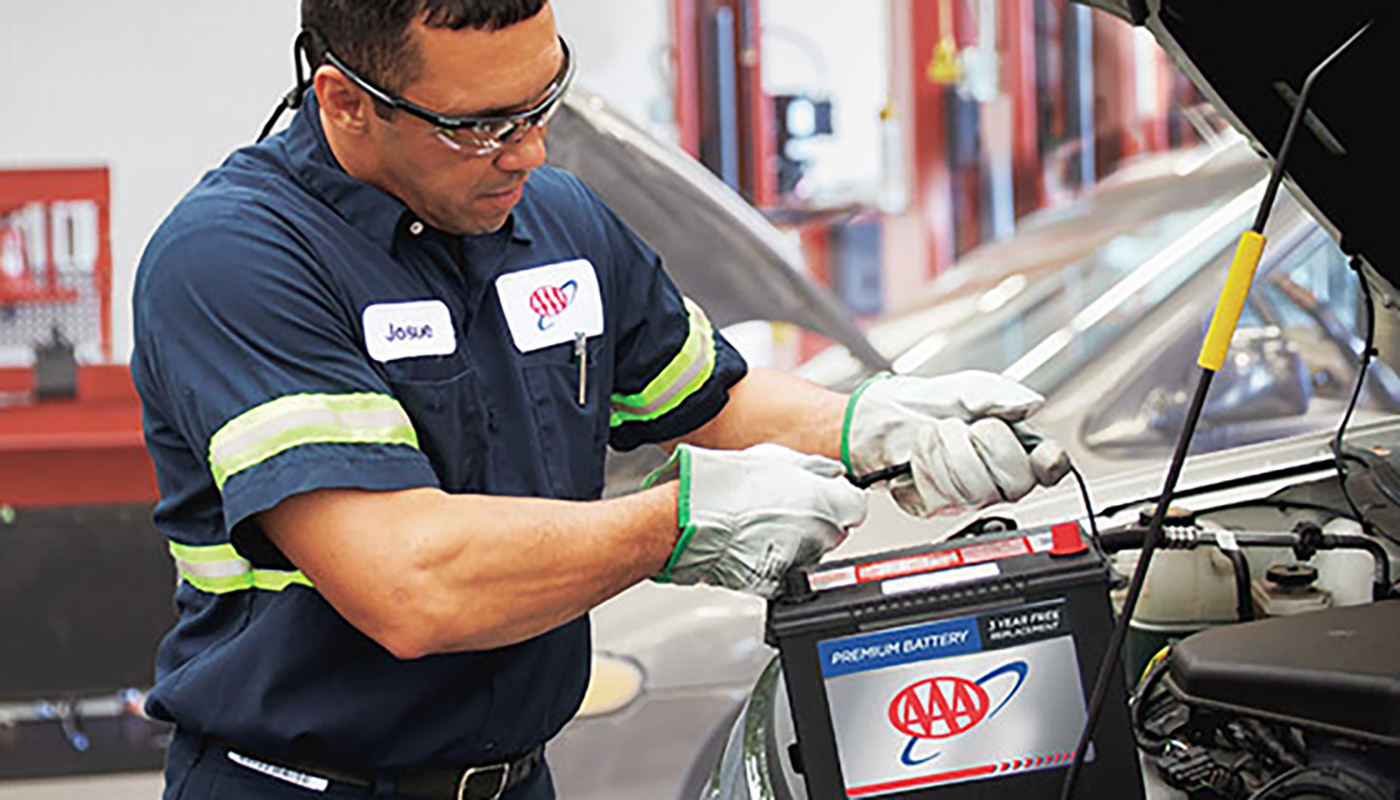 AAA mechanic lowers a new battery into a car.