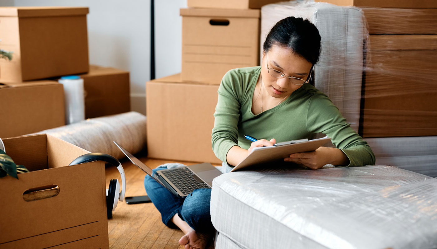 Asian woman going through checklist while using laptop and moving into new home.