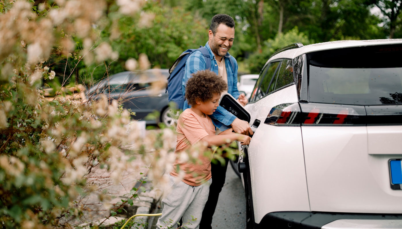 Smiling man with son charging electric car 