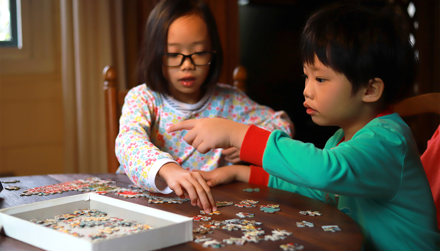 Cute Boy And Girl Playing Jigsaw Puzzle On Wooden Table At Home