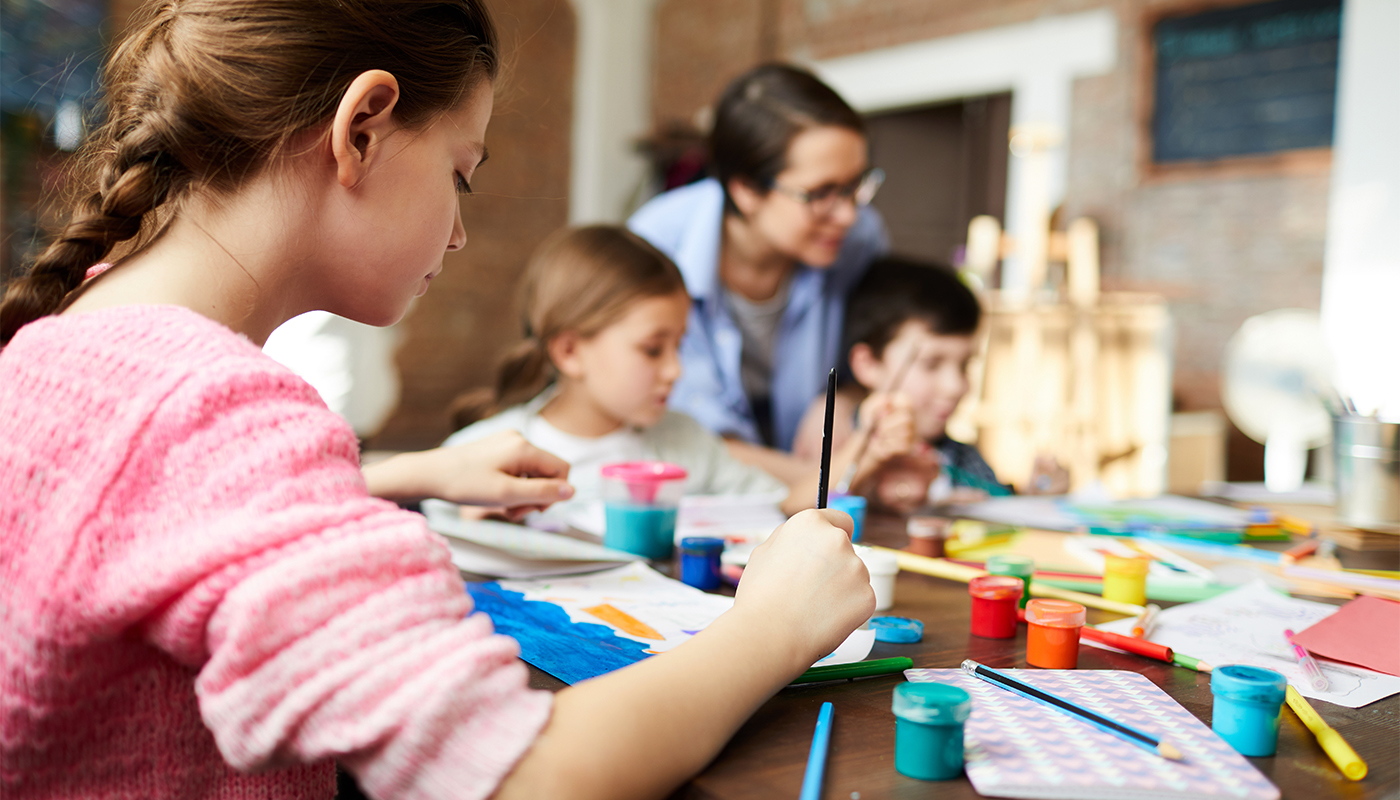 Teenage girl painting picture in art class with group of children