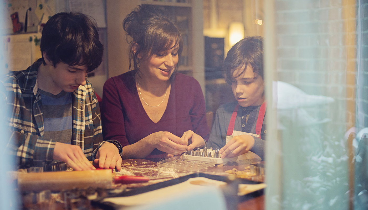 Mother and her two sons making gingerbread holiday cookies at home. Shot through window. 