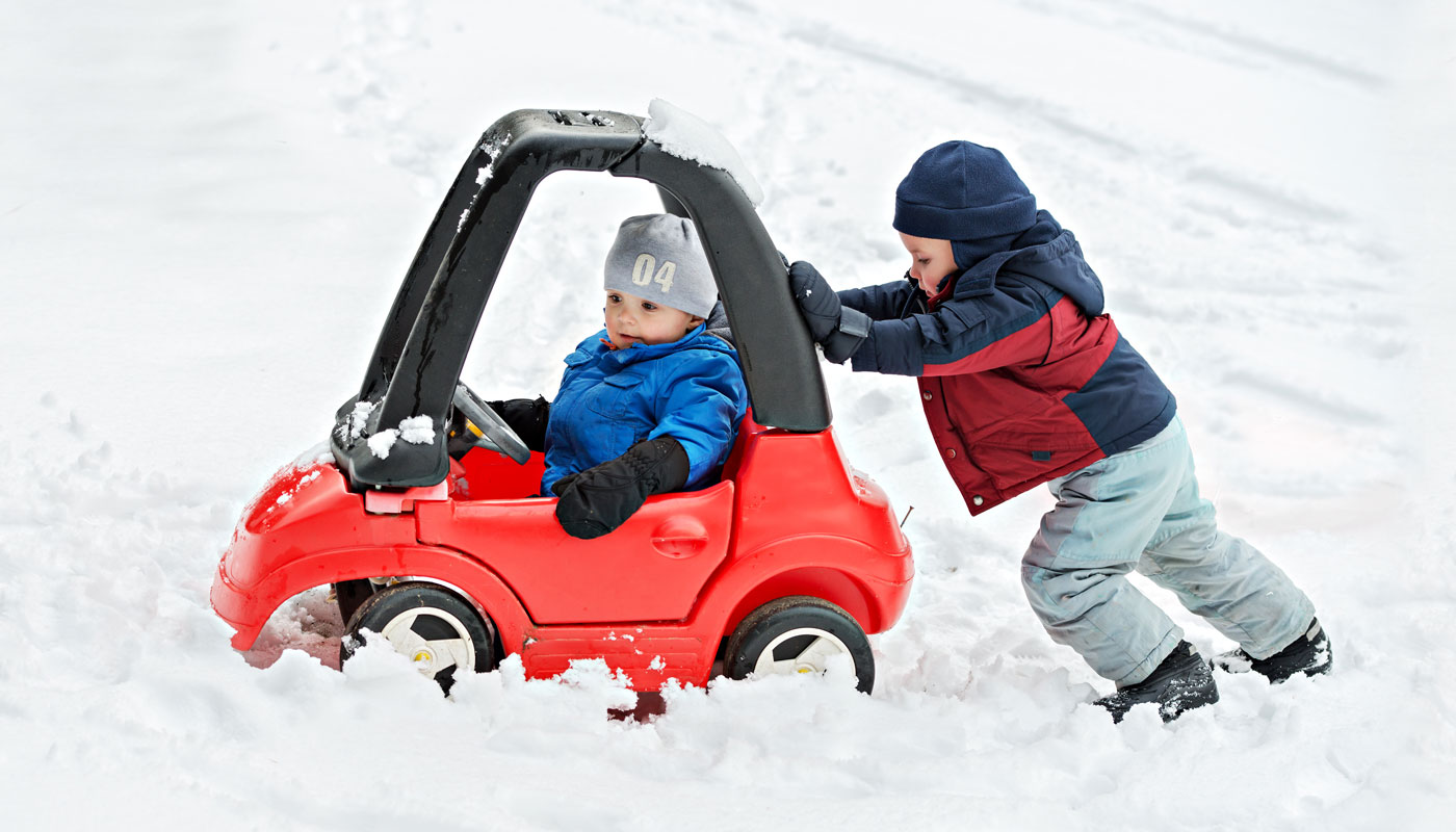 Young Boy Gives a Push to his Brother's Toy Car Stuck in the Snow