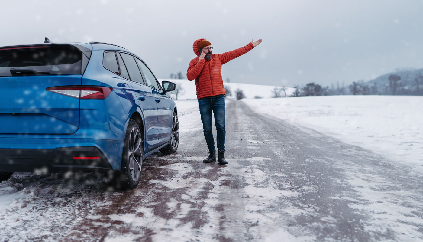 Man standing by car in winter conditions on the phone calling for help, waiting for breakdown service car, tow truck.